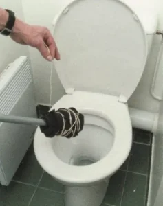 Objeto caseiro improvisado com cabo e panos amarrados tentando desentupir vaso sanitário.